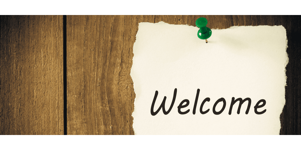 Scrap paper thumb tacked to a wood wall showing word welcome