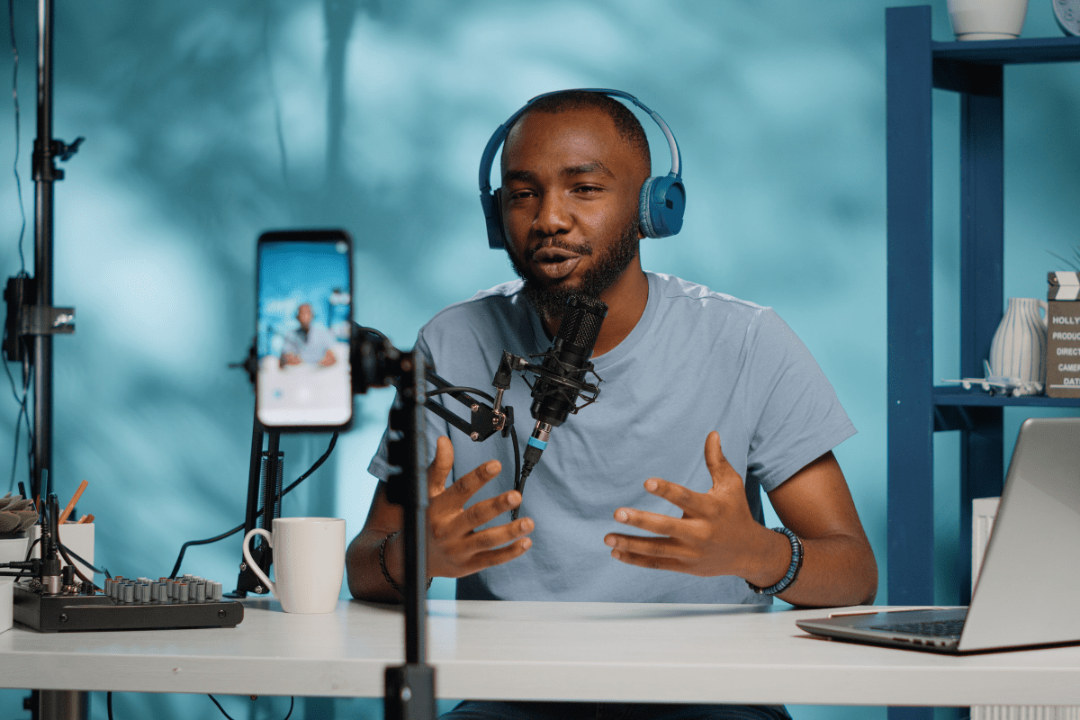 Podcast advertising setup with host recording show using microphone, headphones, and smartphone camera in a professional studio