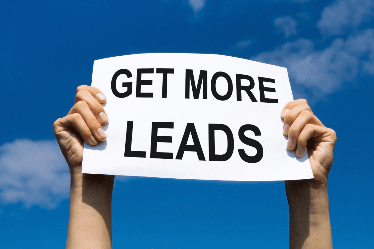 Two hands holding up a white sign with bold black text that reads “GET MORE LEADS” against a bright blue sky with scattered clouds. Two hands holding up a white sign with bold black text that reads “GET MORE LEADS” against a bright blue sky with scattered clouds.